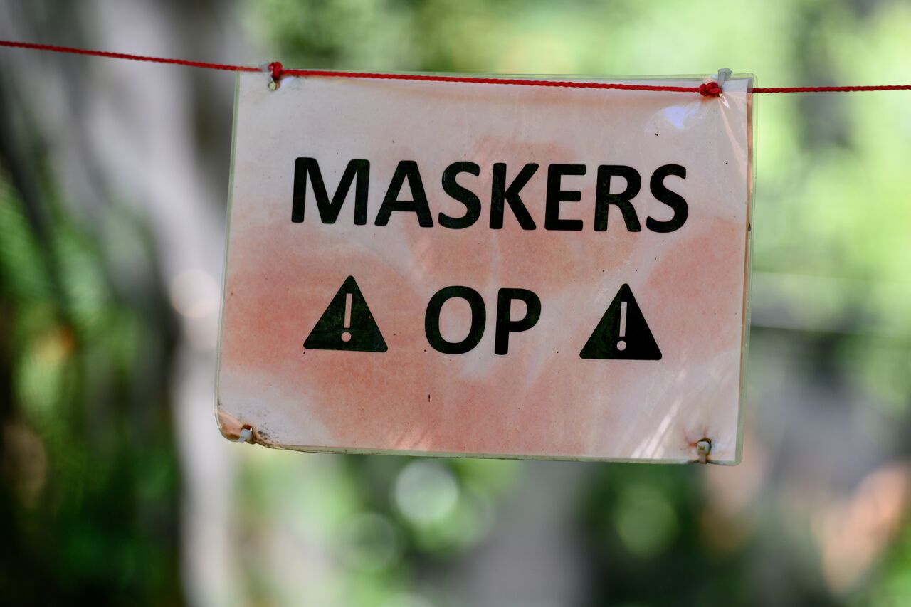 A sign with bold text reads "MASKERS OP!" reminding players to wear masks for safety during paintball.