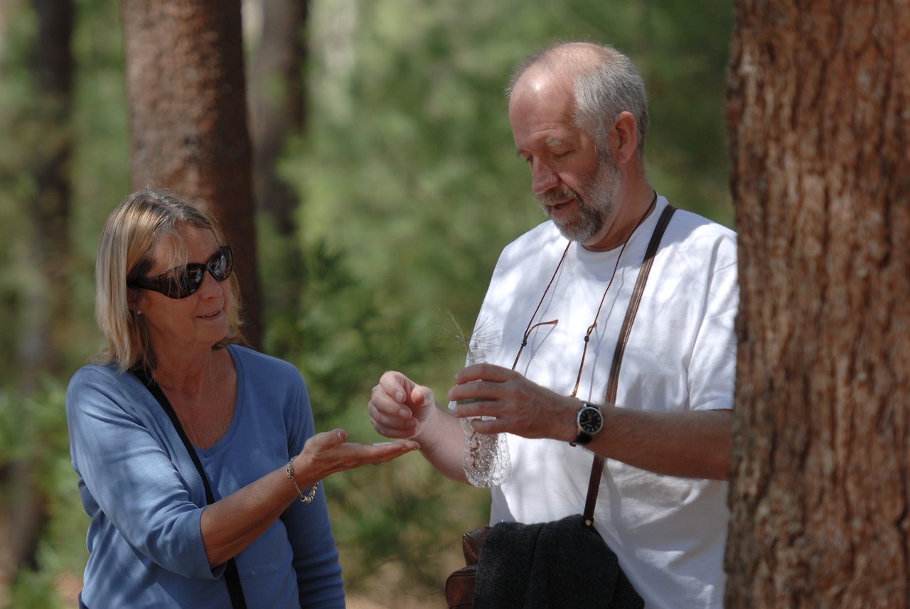 A man pours water from a bottle into a woman's hand while standing on a forest trail.