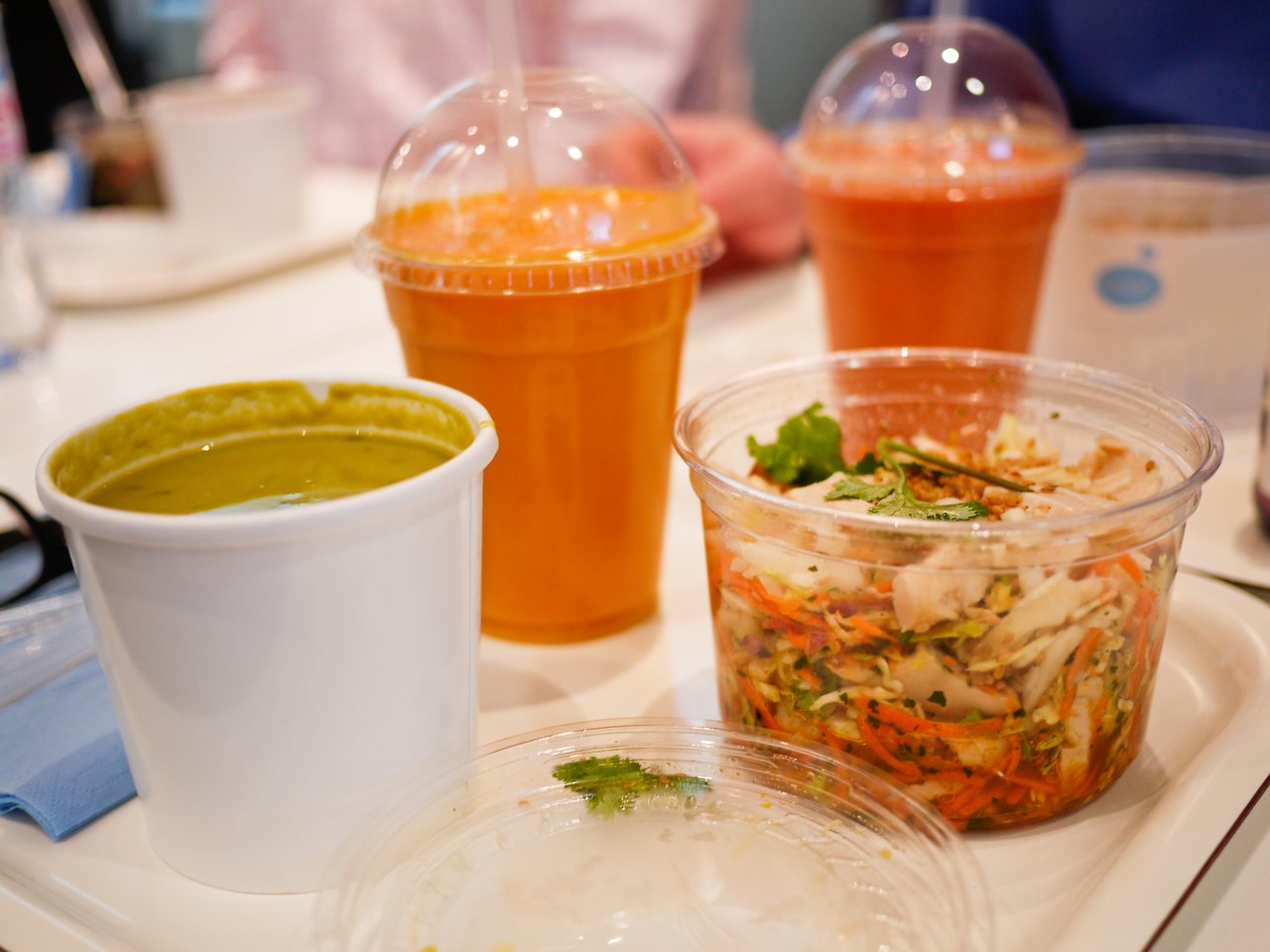 A tray with a salad, green soup, and orange juice in plastic cups at a restaurant table.