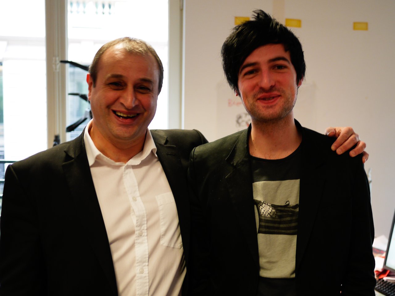 Two men in suits smiling, standing close together.