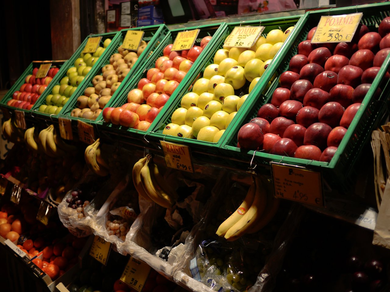 Fresh fruit displayed in green crates at a Paris market stall at night, including apples, bananas, and grapes.