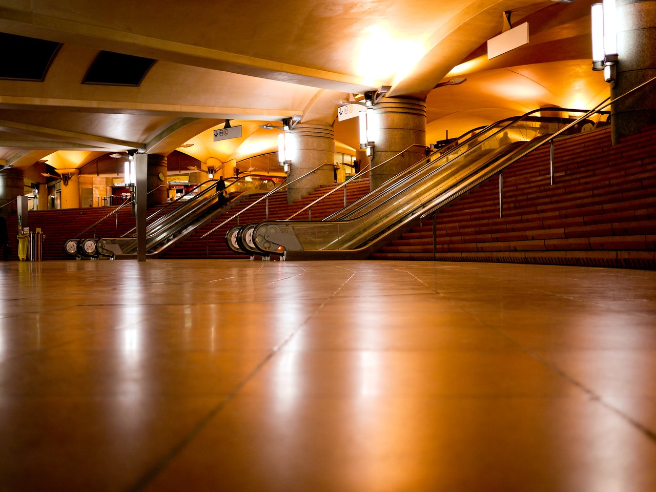A well-lit underground metro station in Paris with escalators and stairs leading to the upper level.
