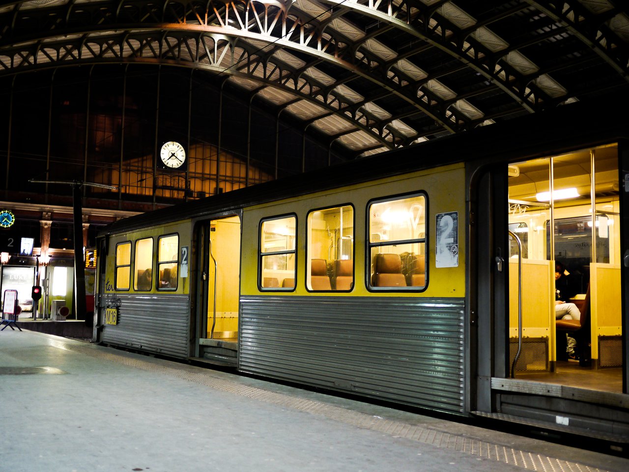A yellow train with open doors is stopped at a well-lit station platform at night in Paris.
