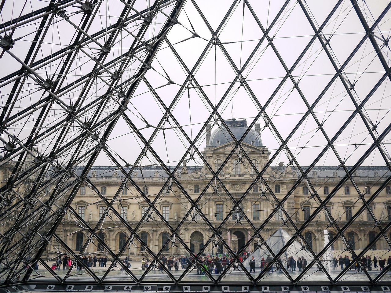 View of the Louvre Museum through the glass pyramid, with visitors walking in the courtyard.