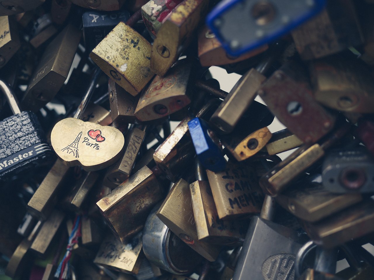 A cluster of love locks attached to a metal structure, with a heart-shaped lock engraved with "Paris" and the Eiffel Tower.