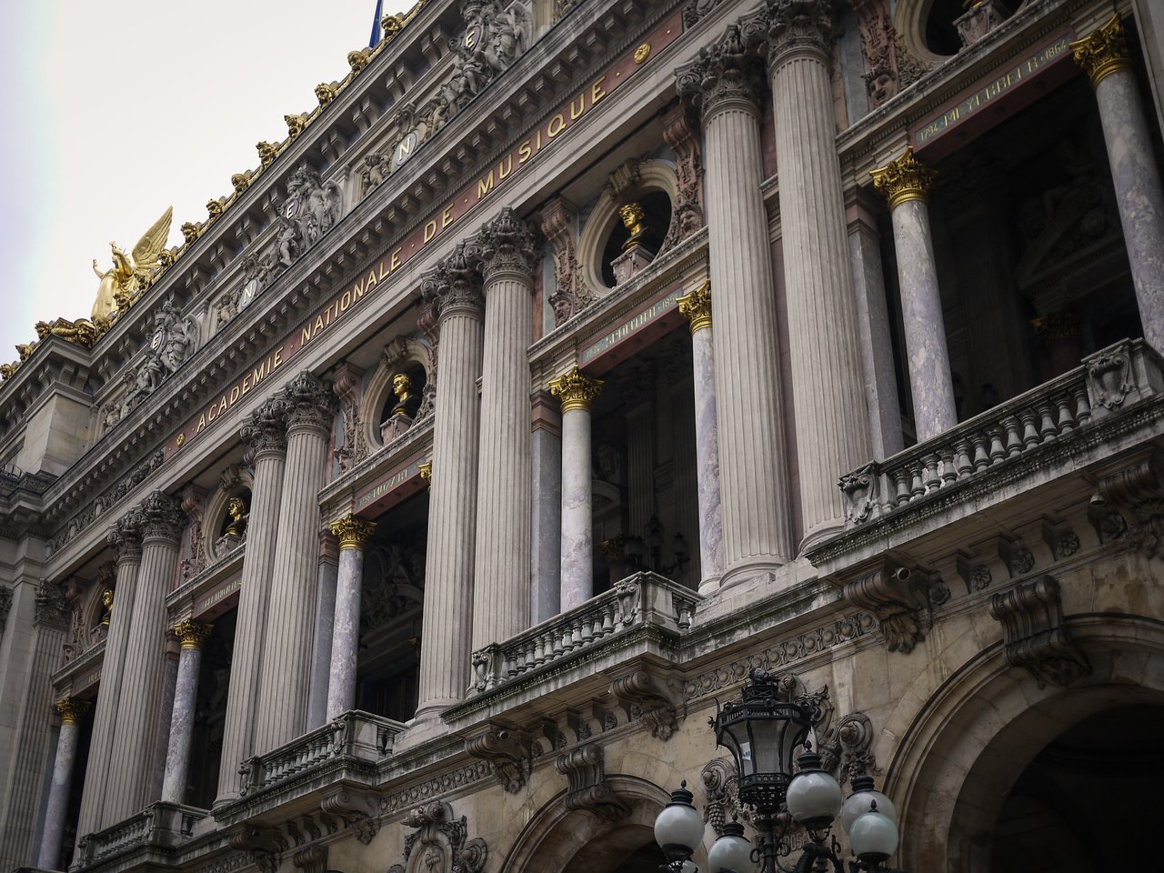The facade of the Palais Garnier in Paris, featuring tall columns, gold accents, and decorative sculptures.
