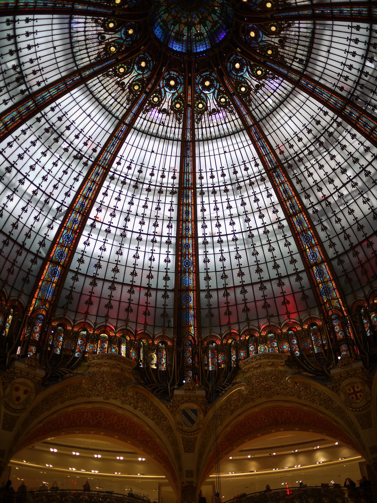 A large stained-glass dome ceiling with intricate patterns and colorful details inside a grand building.