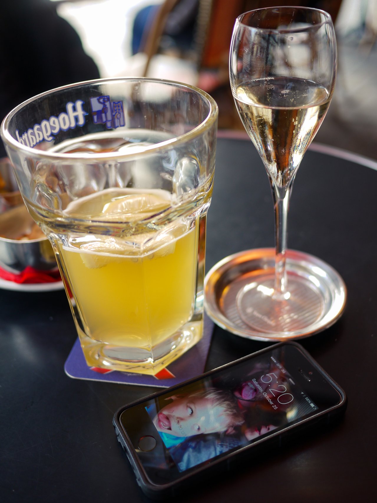A glass of beer, a glass of champagne, and a smartphone on a café table.