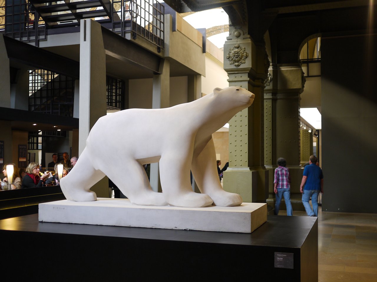 A large white polar bear sculpture stands on display inside a museum, with visitors walking nearby.