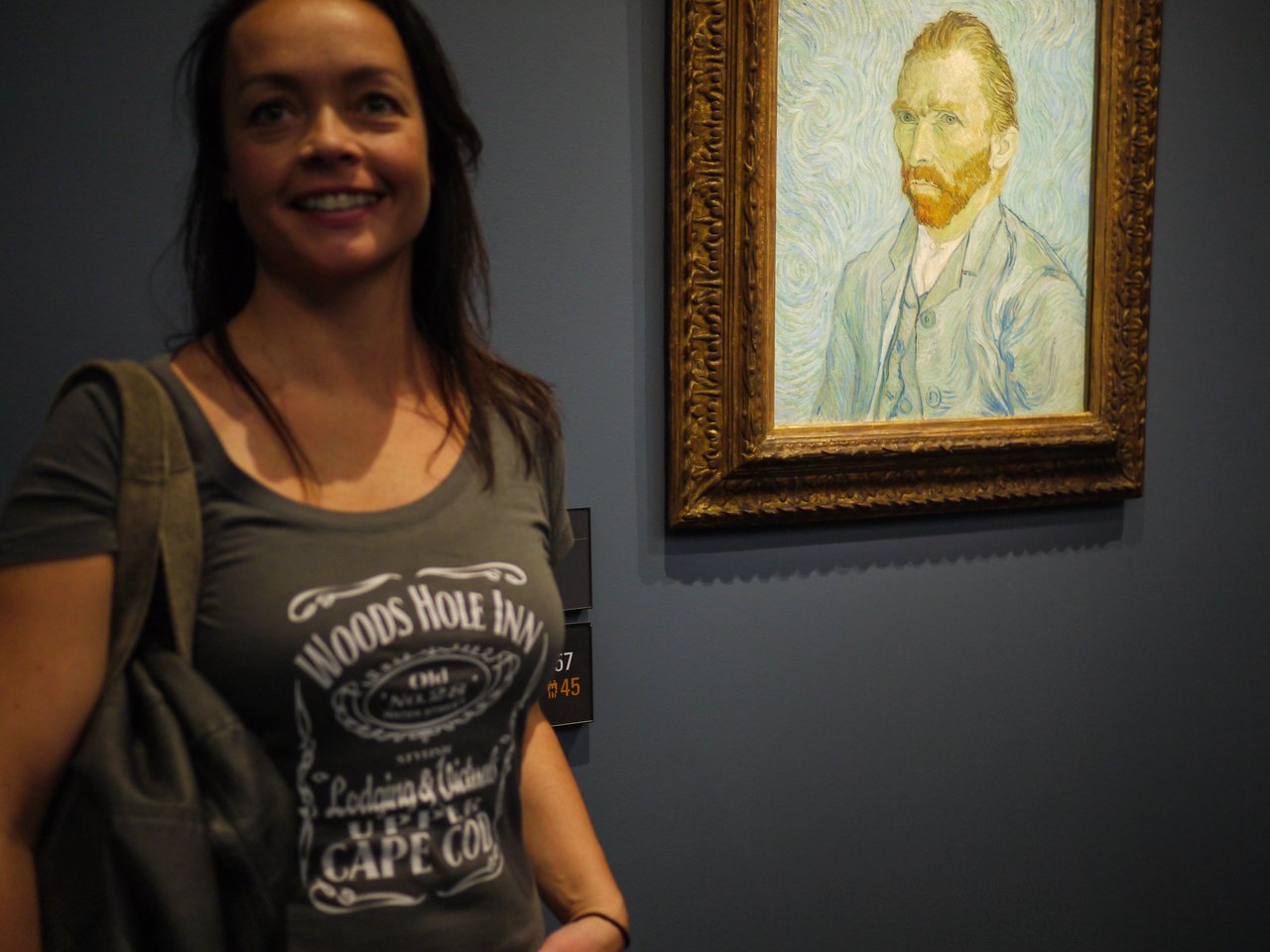 A woman stands next to a framed portrait of Vincent van Gogh in a museum.