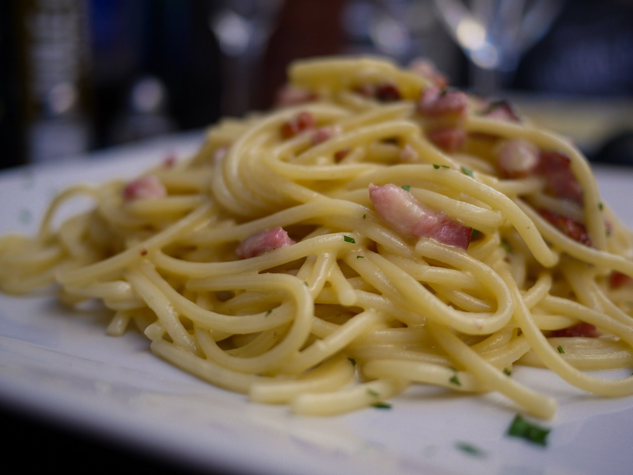 A plate of spaghetti carbonara with bacon and herbs on a white dish.