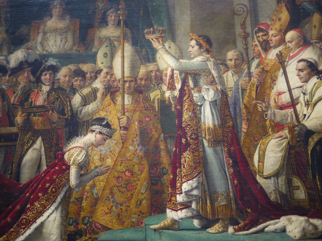 A man in royal attire places a crown on a kneeling woman's head, surrounded by clergy and officials.