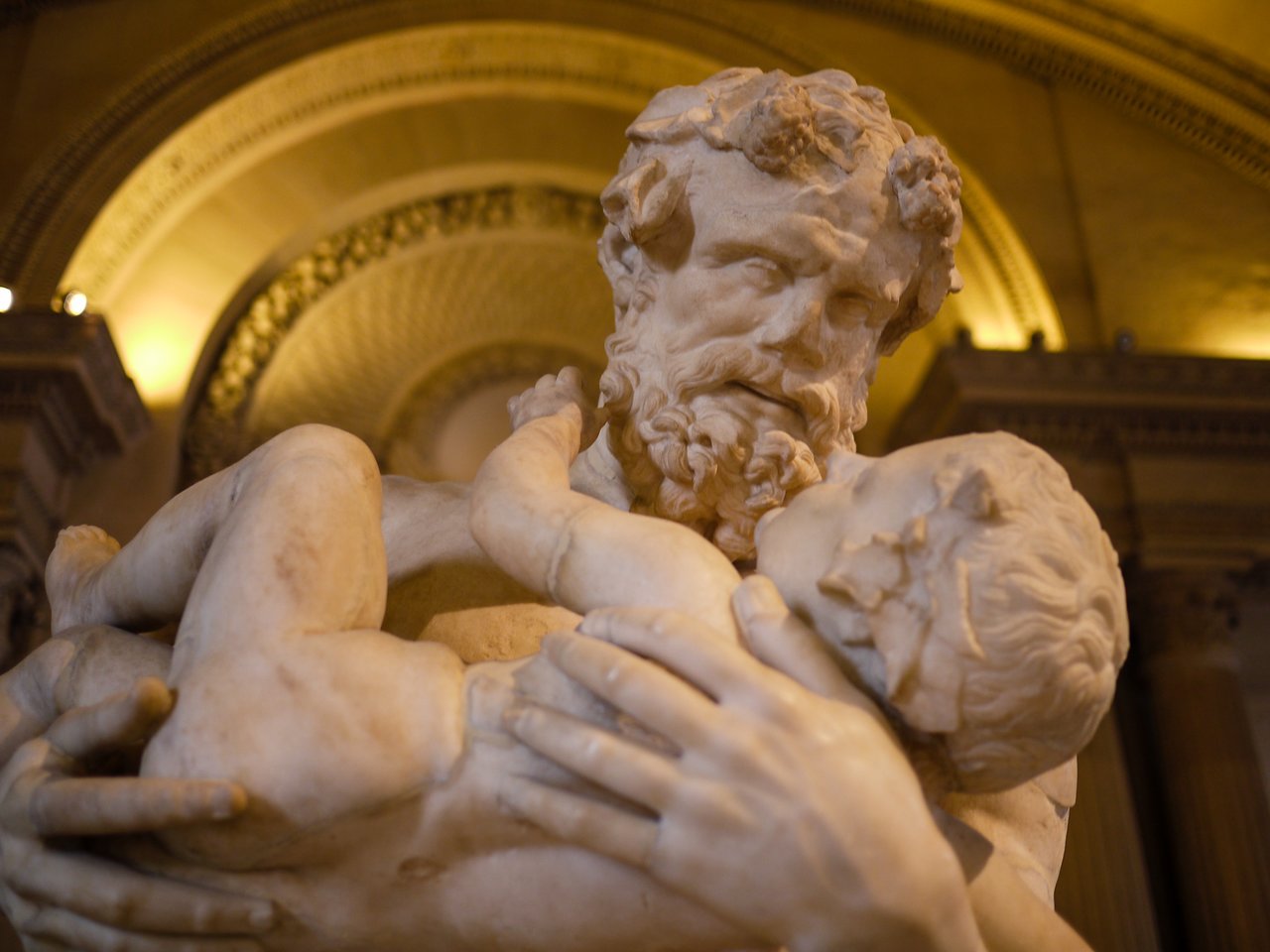 A marble statue of a bearded man holding a child in his arms, both with expressive facial details.