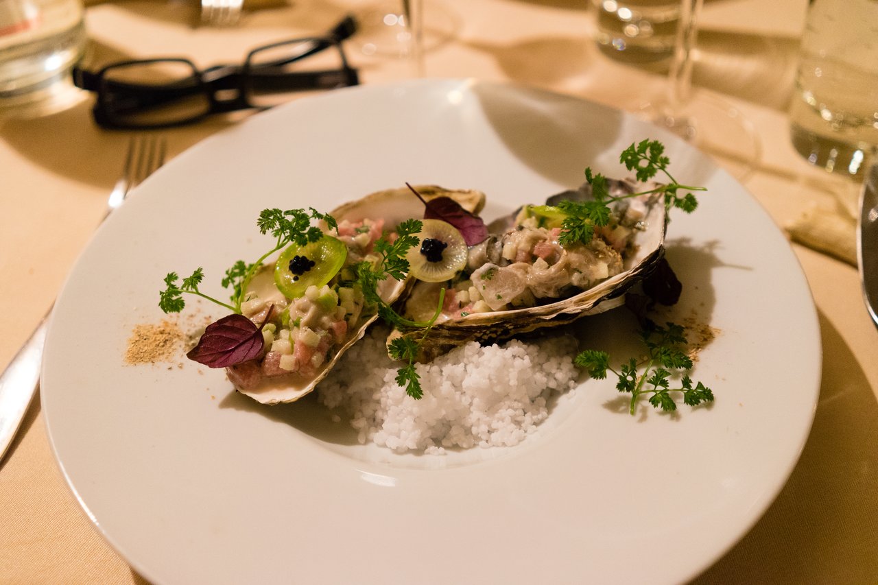 A plate with two oyster shells filled with a seafood mixture, garnished with herbs and caviar, on a table.