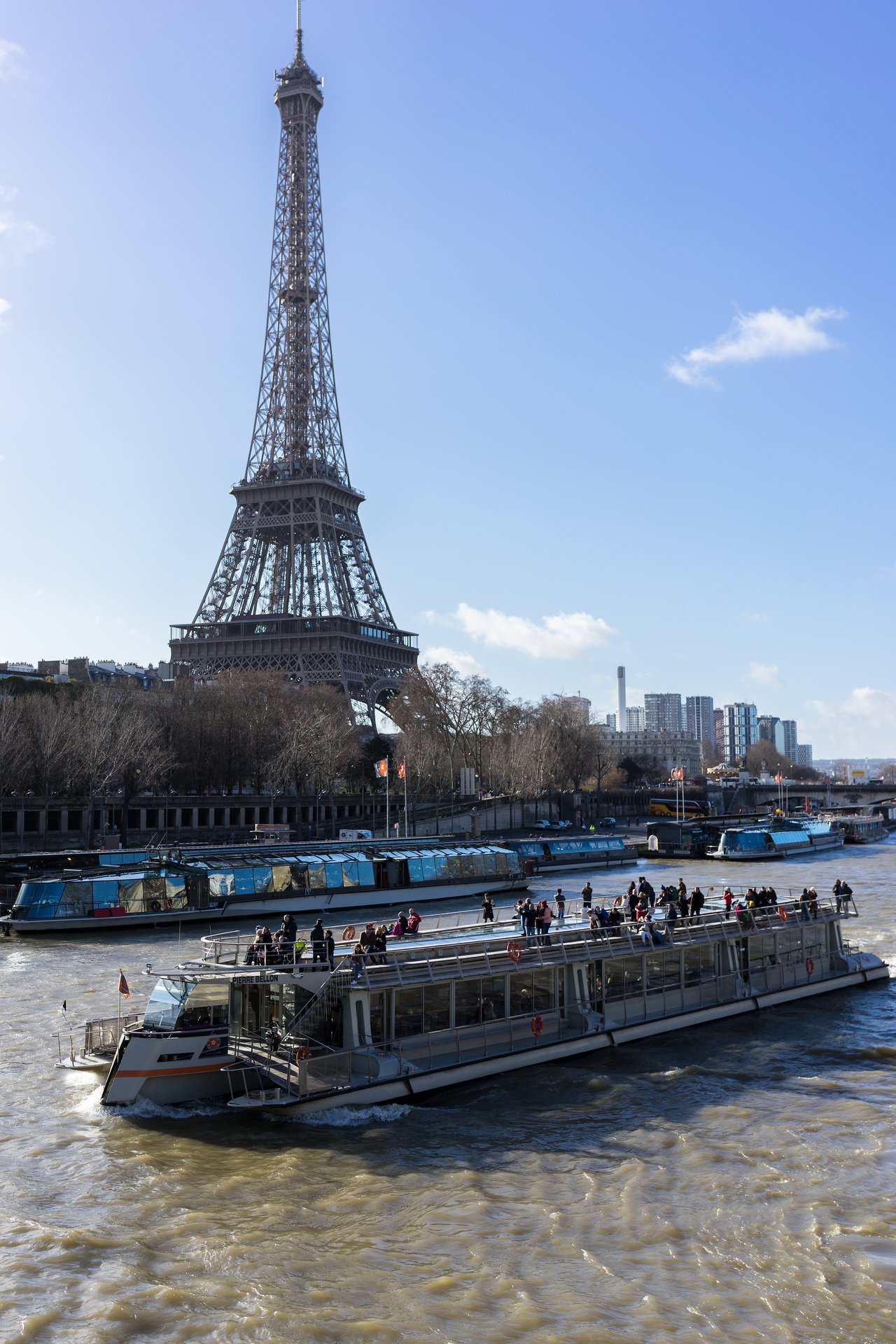 A sightseeing boat with passengers moves along the Seine River, with the Eiffel Tower in the background.