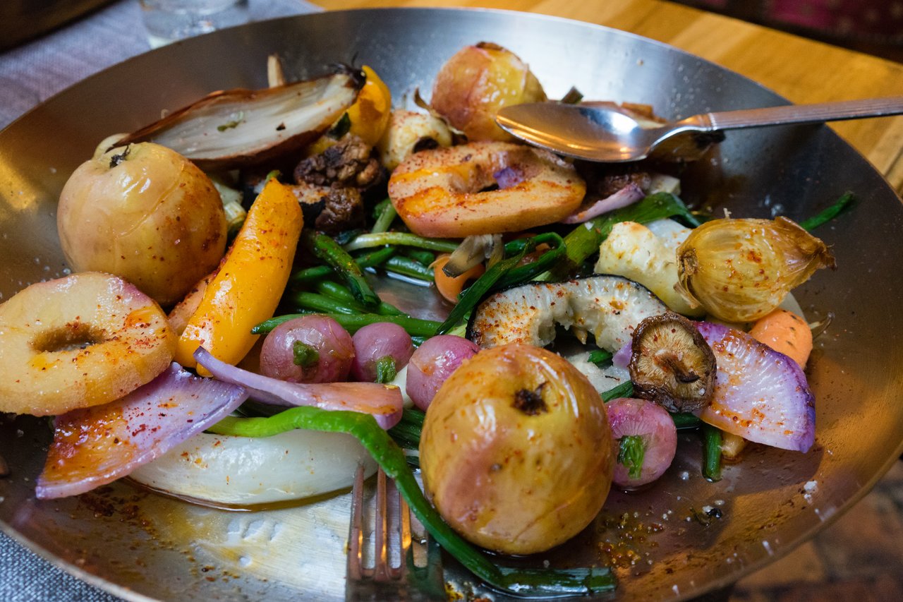 A metal plate filled with roasted vegetables, including onions, radishes, and mushrooms, with a spoon and fork resting inside.