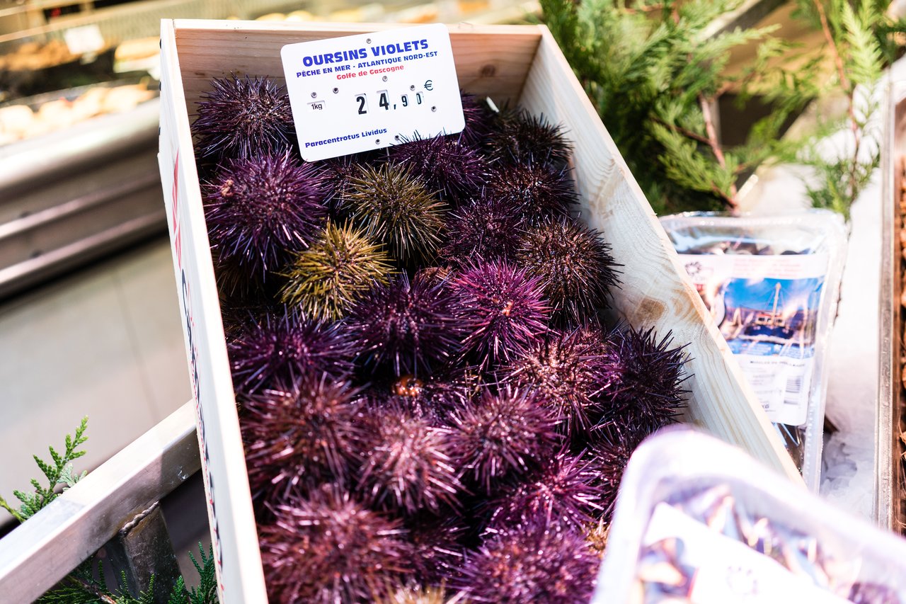 A wooden crate filled with purple sea urchins for sale at a seafood market, with a price sign.