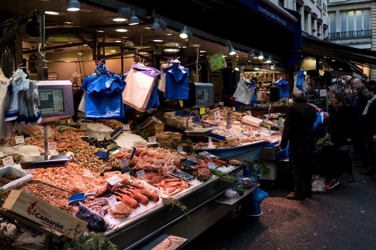 A seafood market in Paris with fresh fish, shrimp, and lobster on display as people browse and shop.