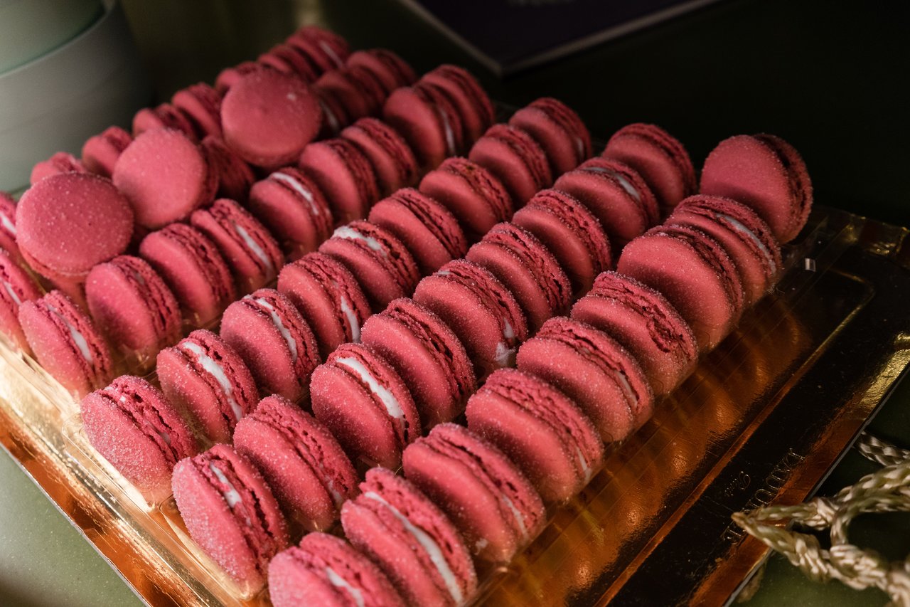 A tray of neatly arranged pink macarons with white filling, displayed on a golden surface.