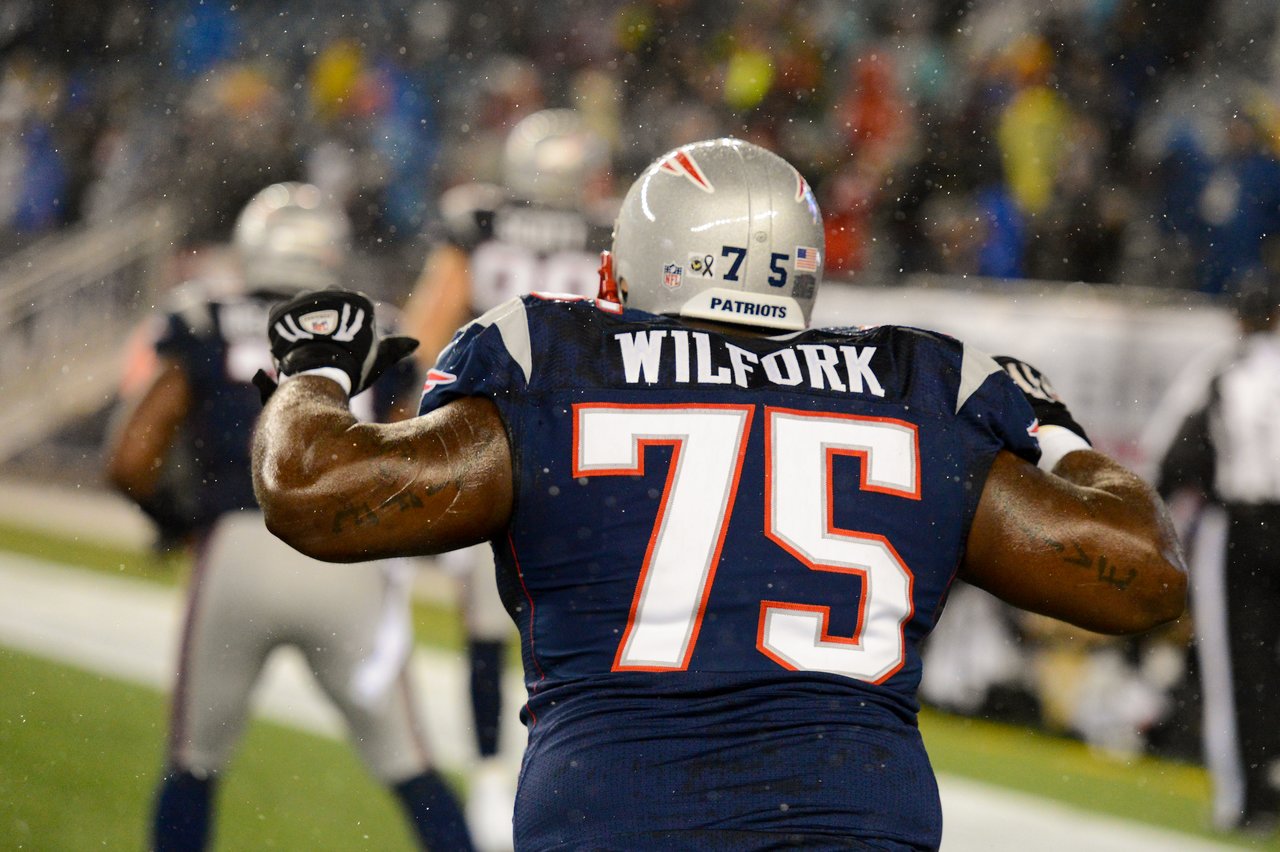 A Patriots player wearing jersey number 75 flexes his arms during a game in the rain.