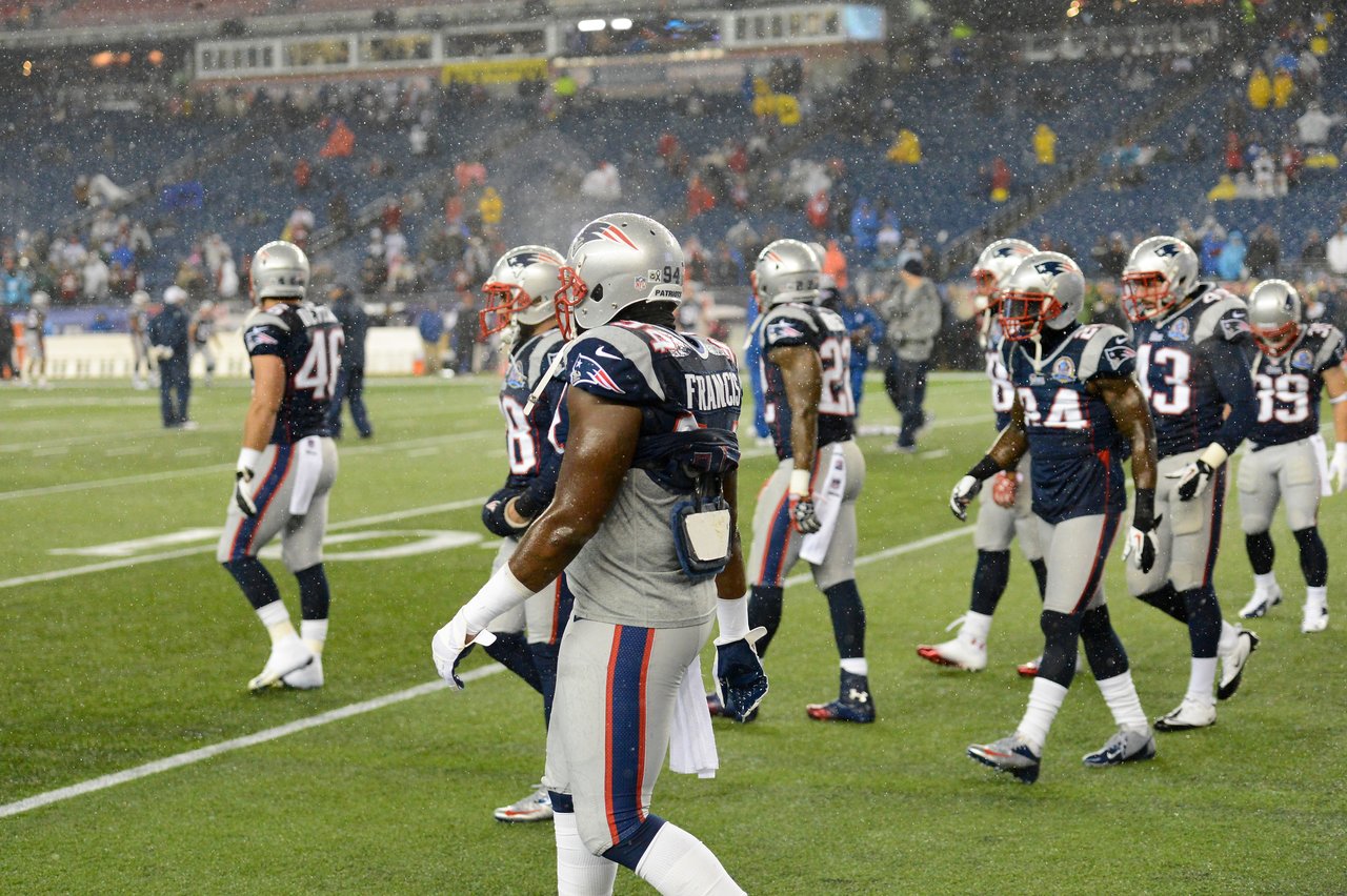 New England Patriots players walk on the field during a game in rainy weather.
