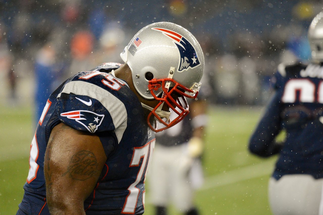 A New England Patriots player in a helmet looks down during a game in the rain.