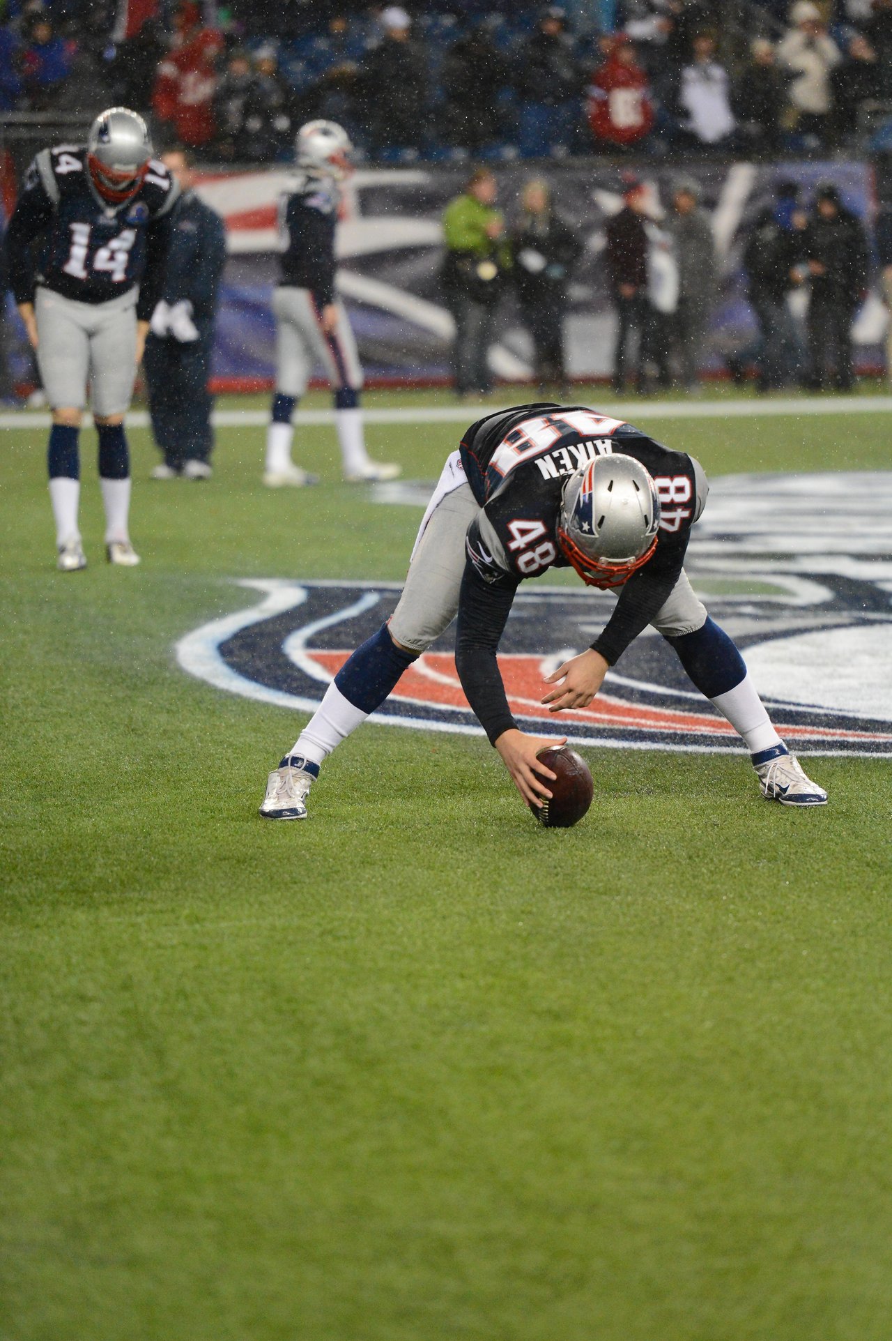 A Patriots player in a football uniform prepares to snap the ball during a game.