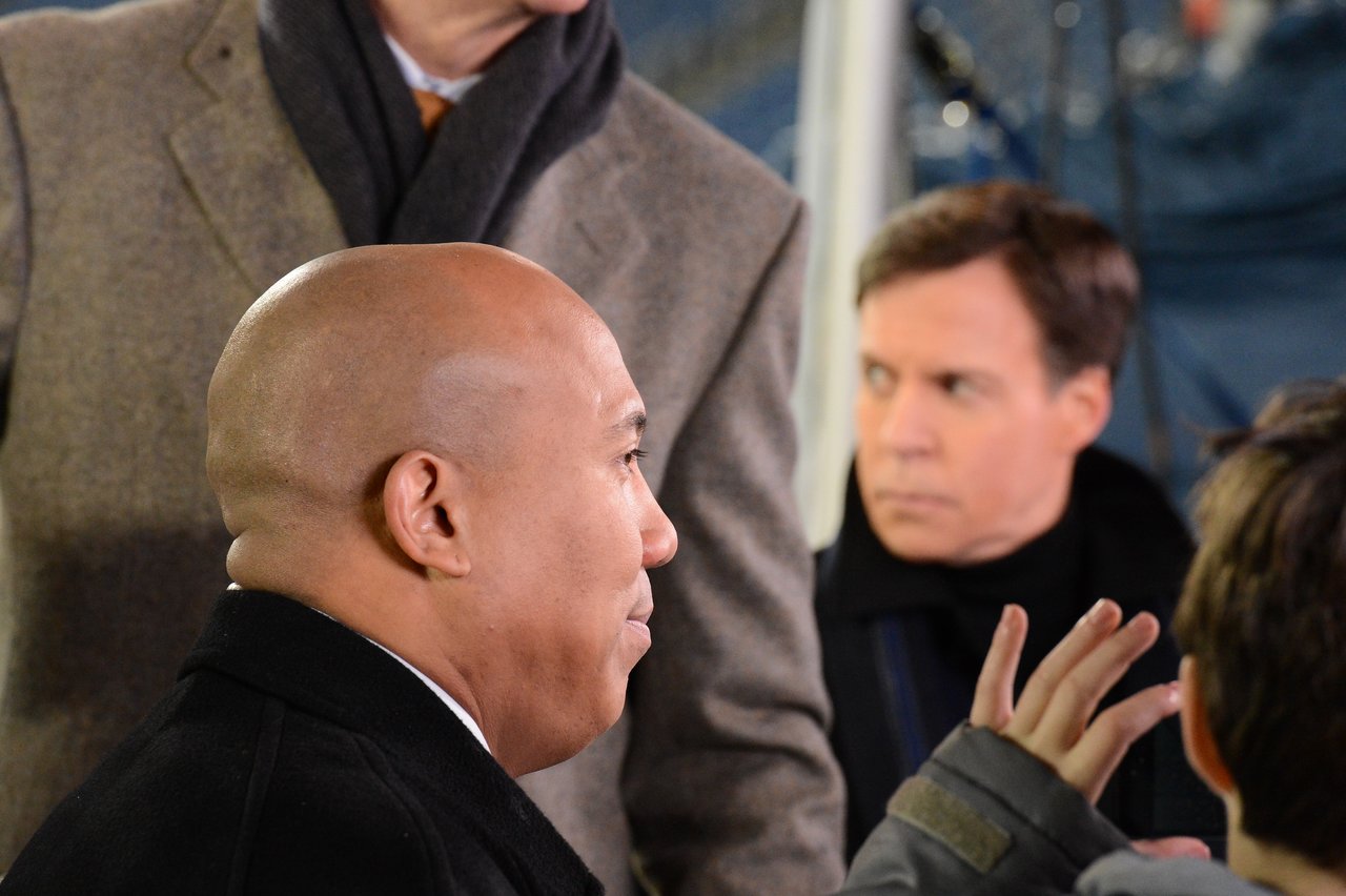 A man in a black coat listens while a child raises a hand.