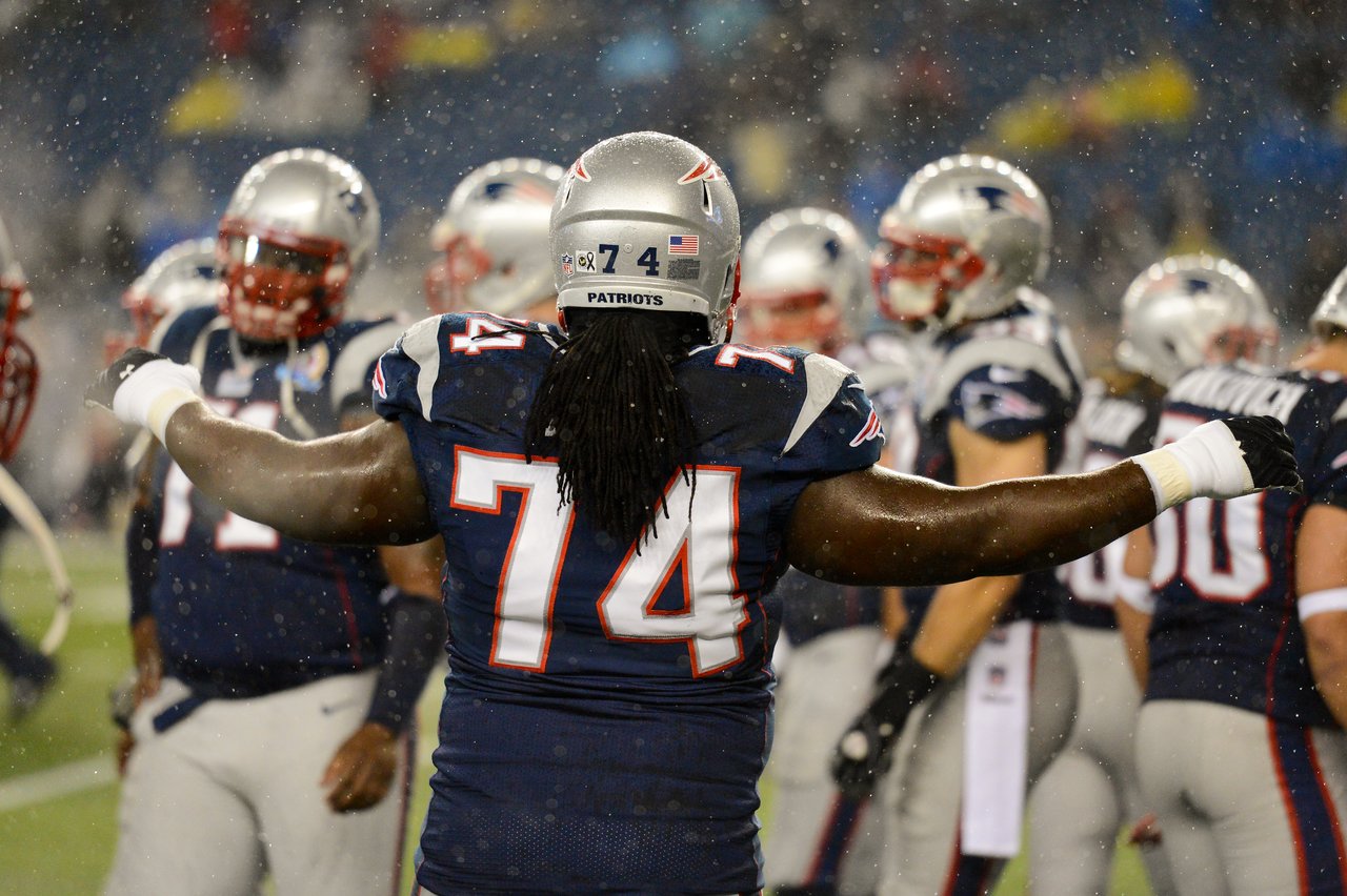 A Patriots player wearing number 74 stands with arms outstretched during a game in the rain.