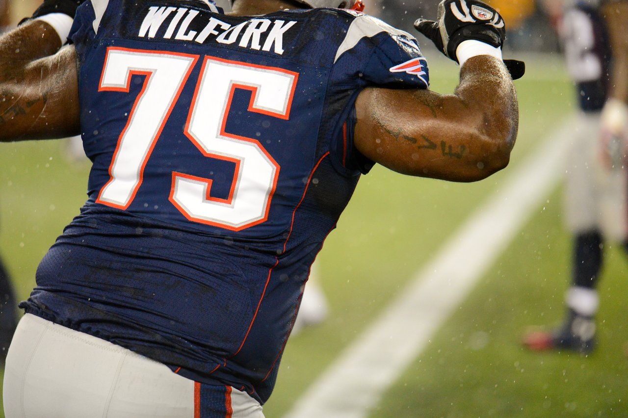 A football player in a Patriots jersey with number 75 moves on the field during a game in the rain.