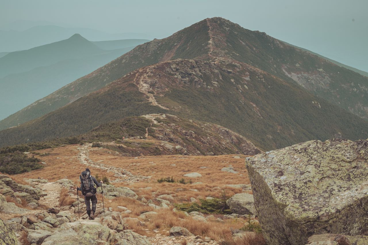 A hiker trekking on a ridge towards a mountain peak.
