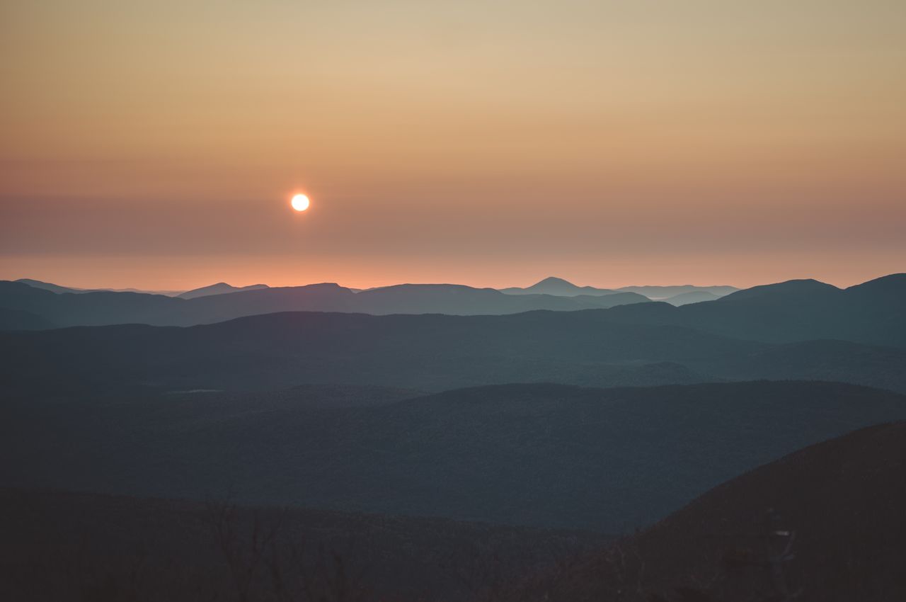 The sun rising over layered mountains, fading from dark to light shades of gray.