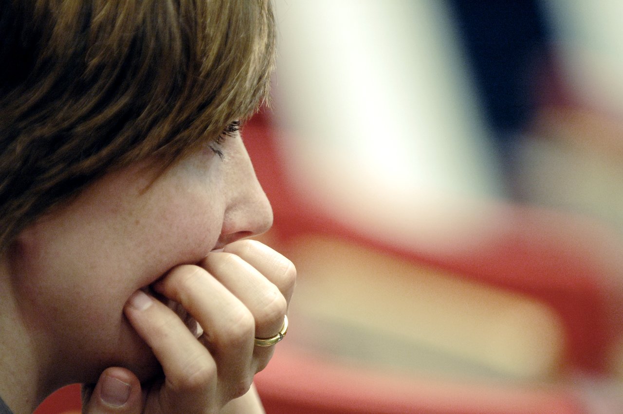 A person with short brown hair rests their chin on their hand, appearing focused while looking ahead.
