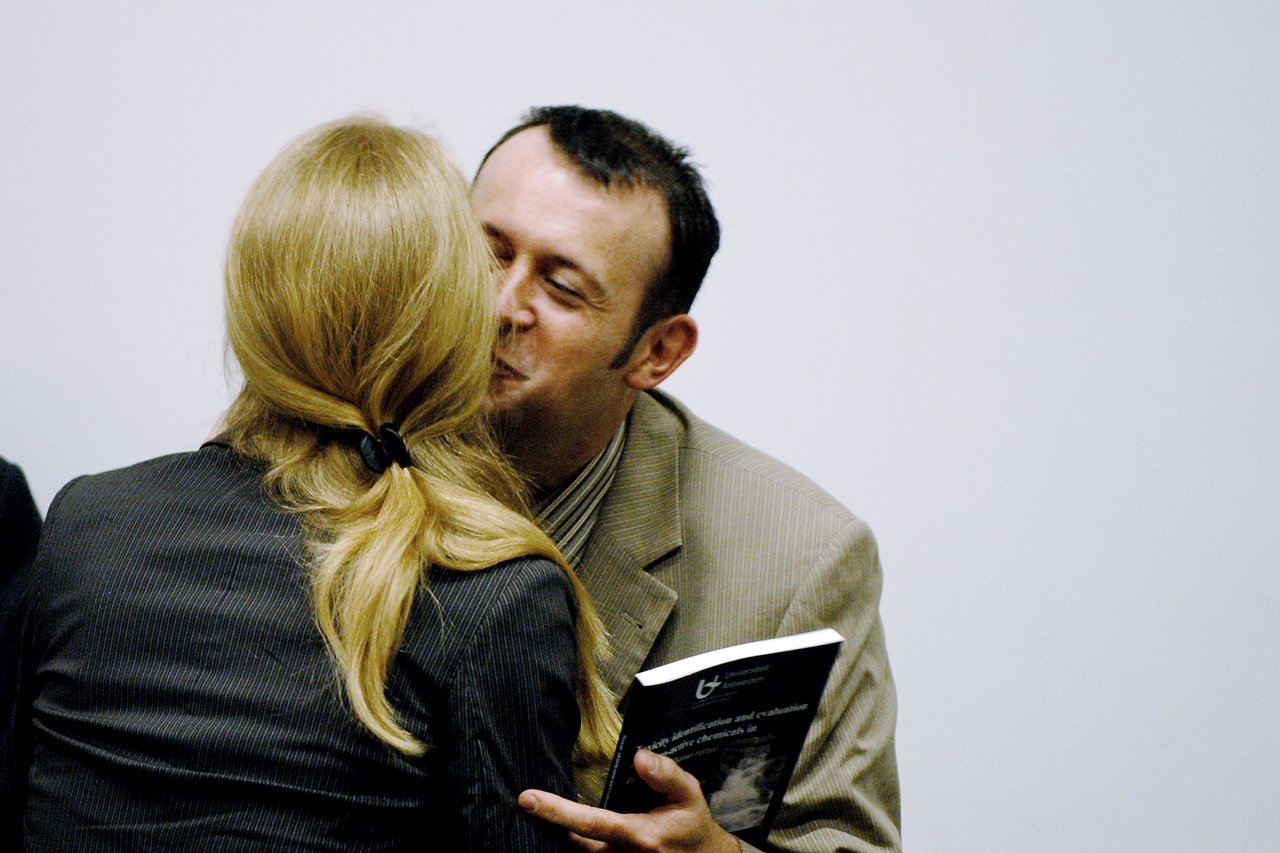 A man in a suit kisses a woman on the cheek while holding a book, congratulating her.