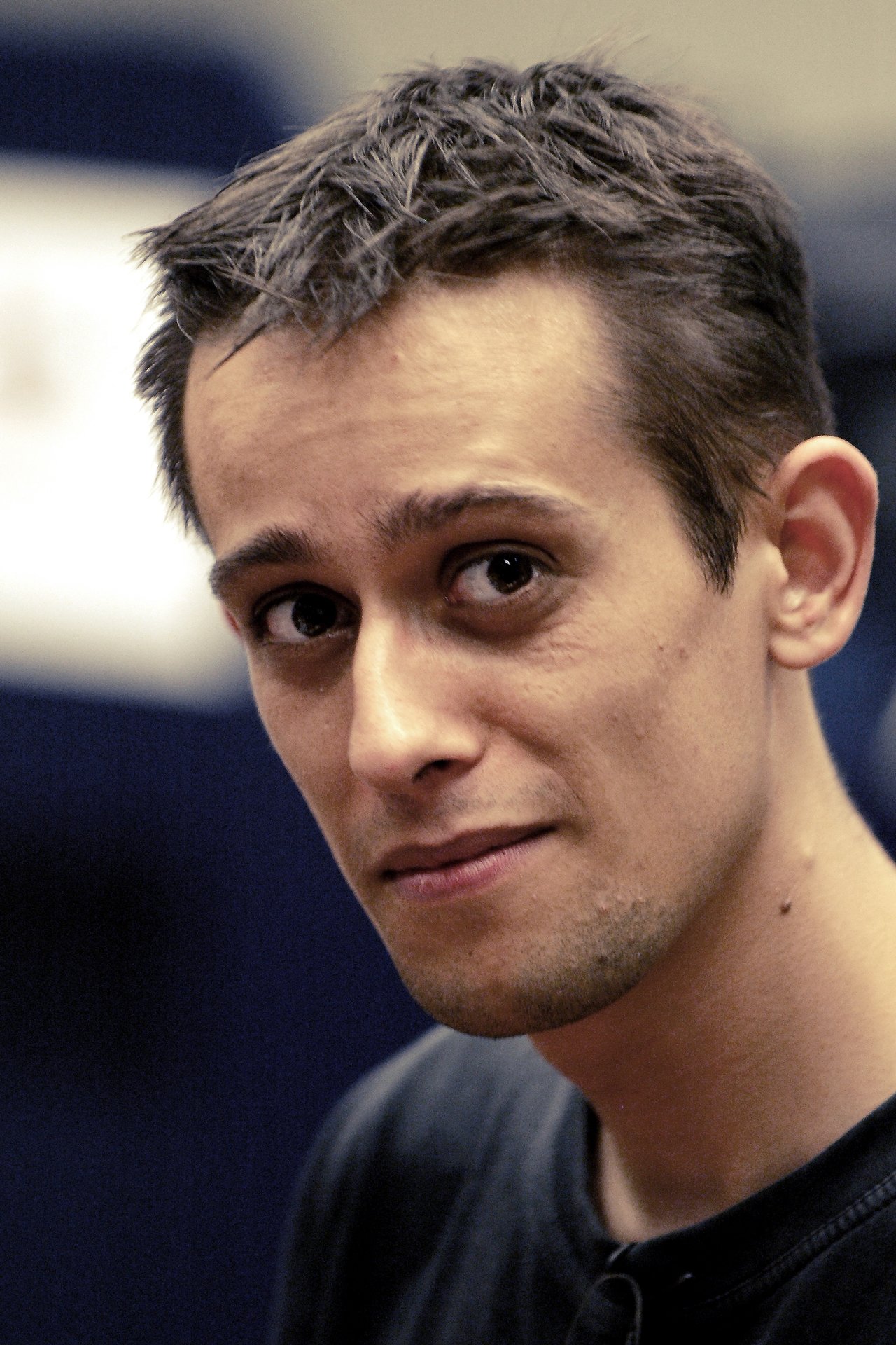 A man with short dark hair and a black shirt looks at the camera with a slight smile.