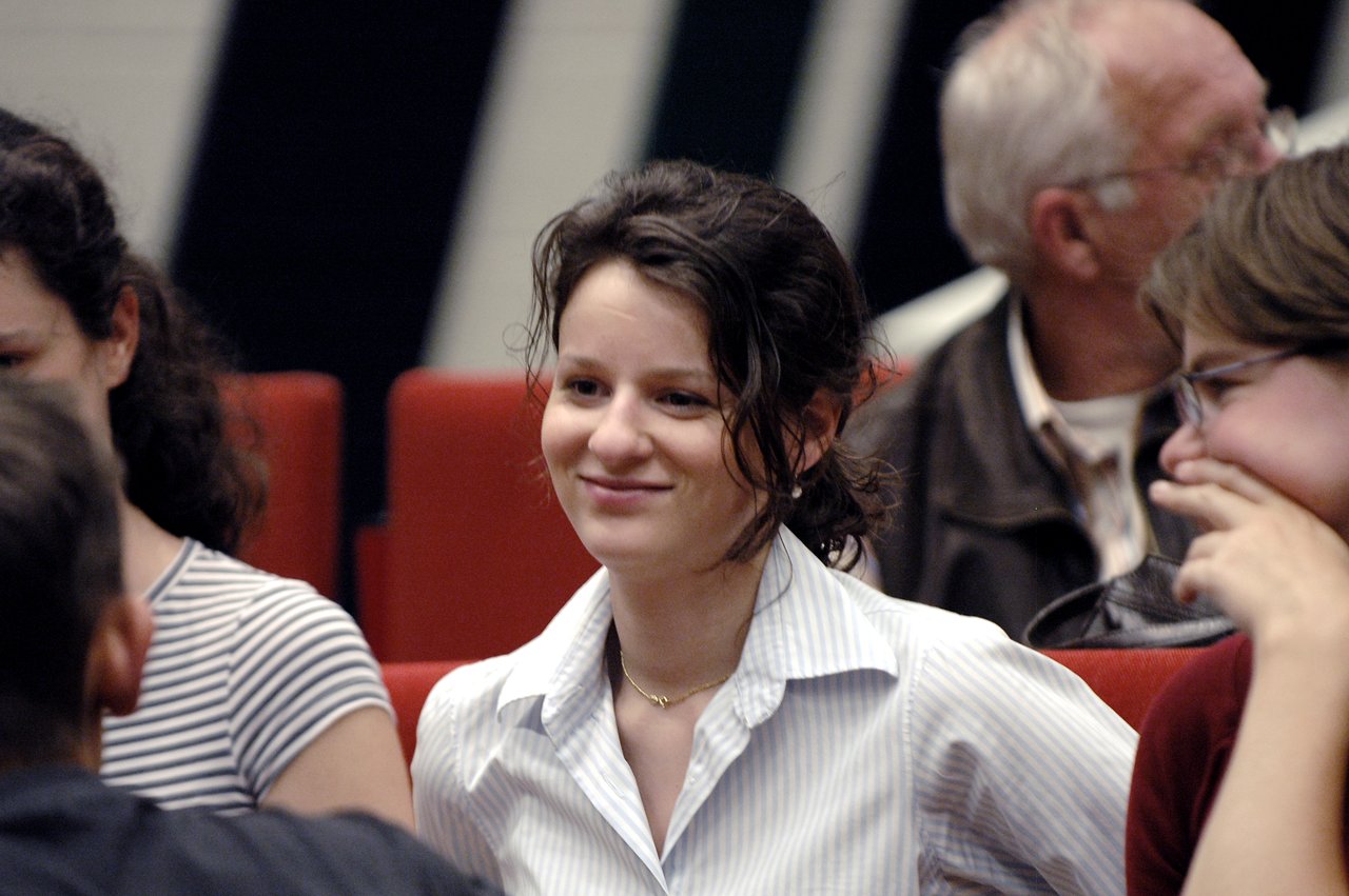 A woman in a striped shirt smiles while sitting among others in a lecture hall.