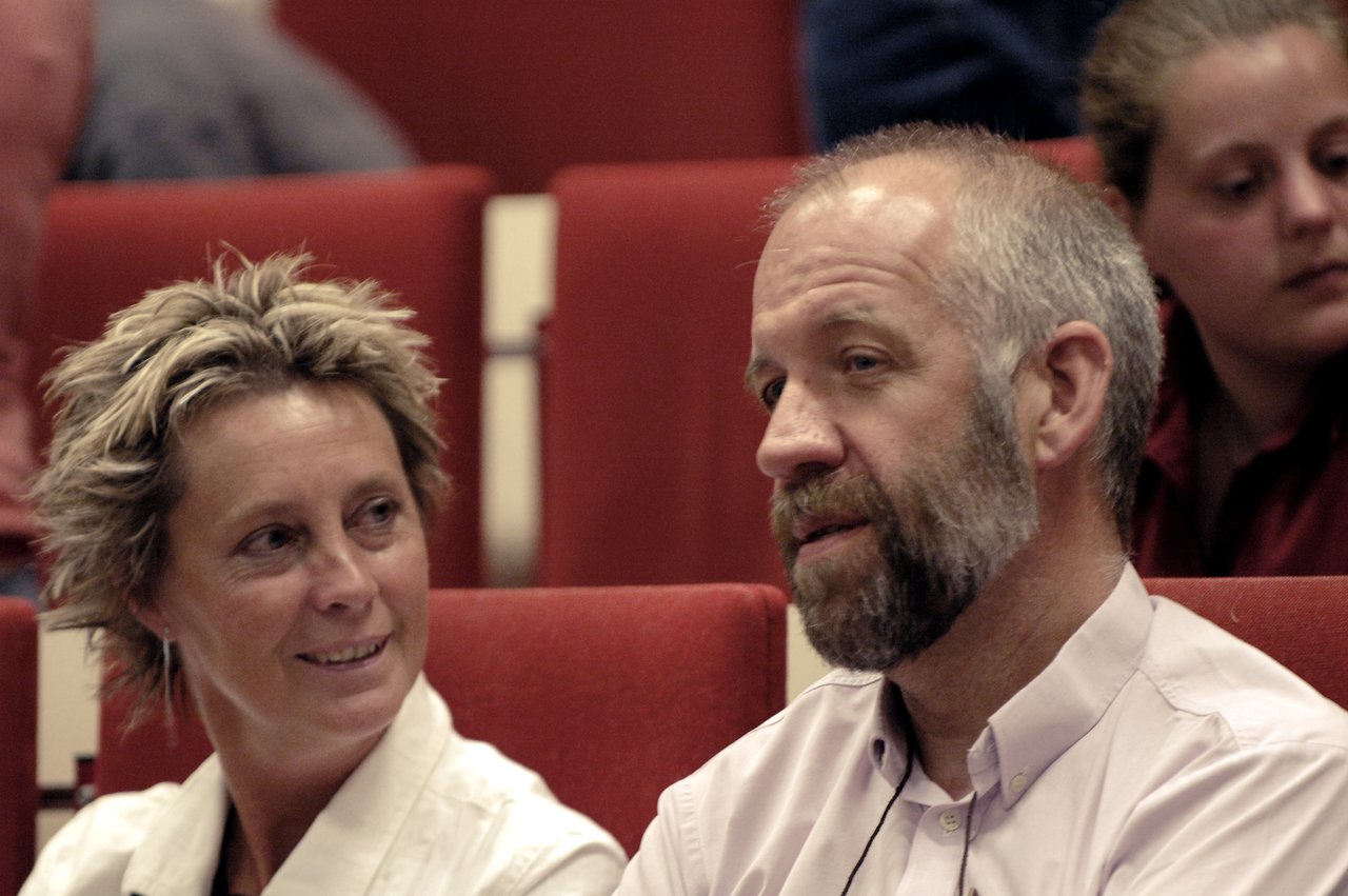 A man and a woman sit in red auditorium chairs, engaged in conversation.