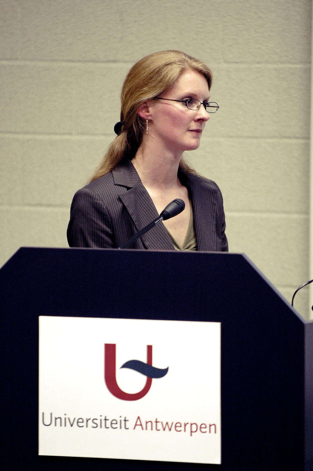A woman speaks into a microphone at a podium during a presentation at the University of Antwerp.