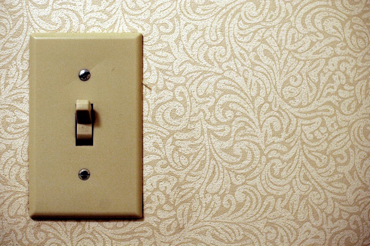 A beige light switch in the "on" position, mounted on a patterned wall with a matching cover plate.