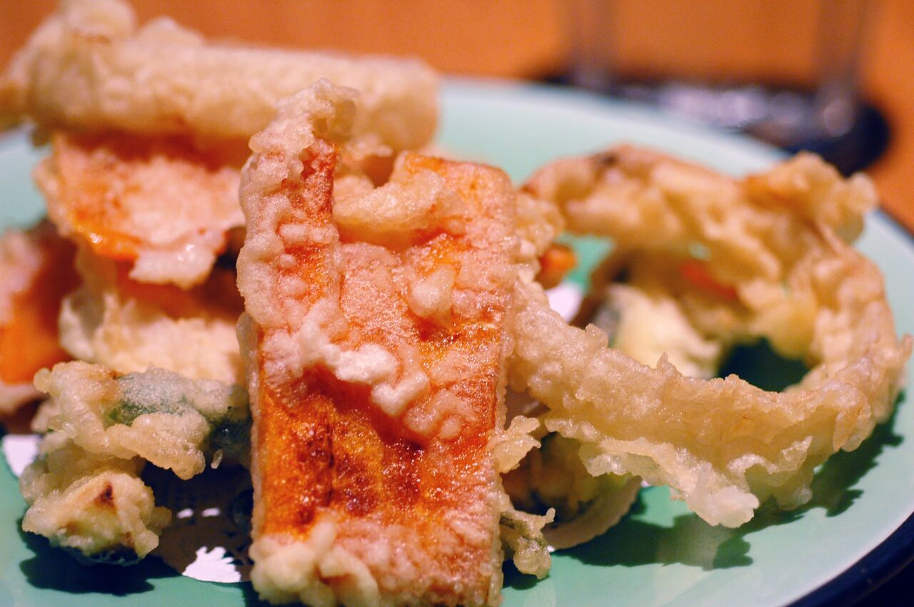 A plate of assorted tempura with battered and fried vegetables, served on a green dish.