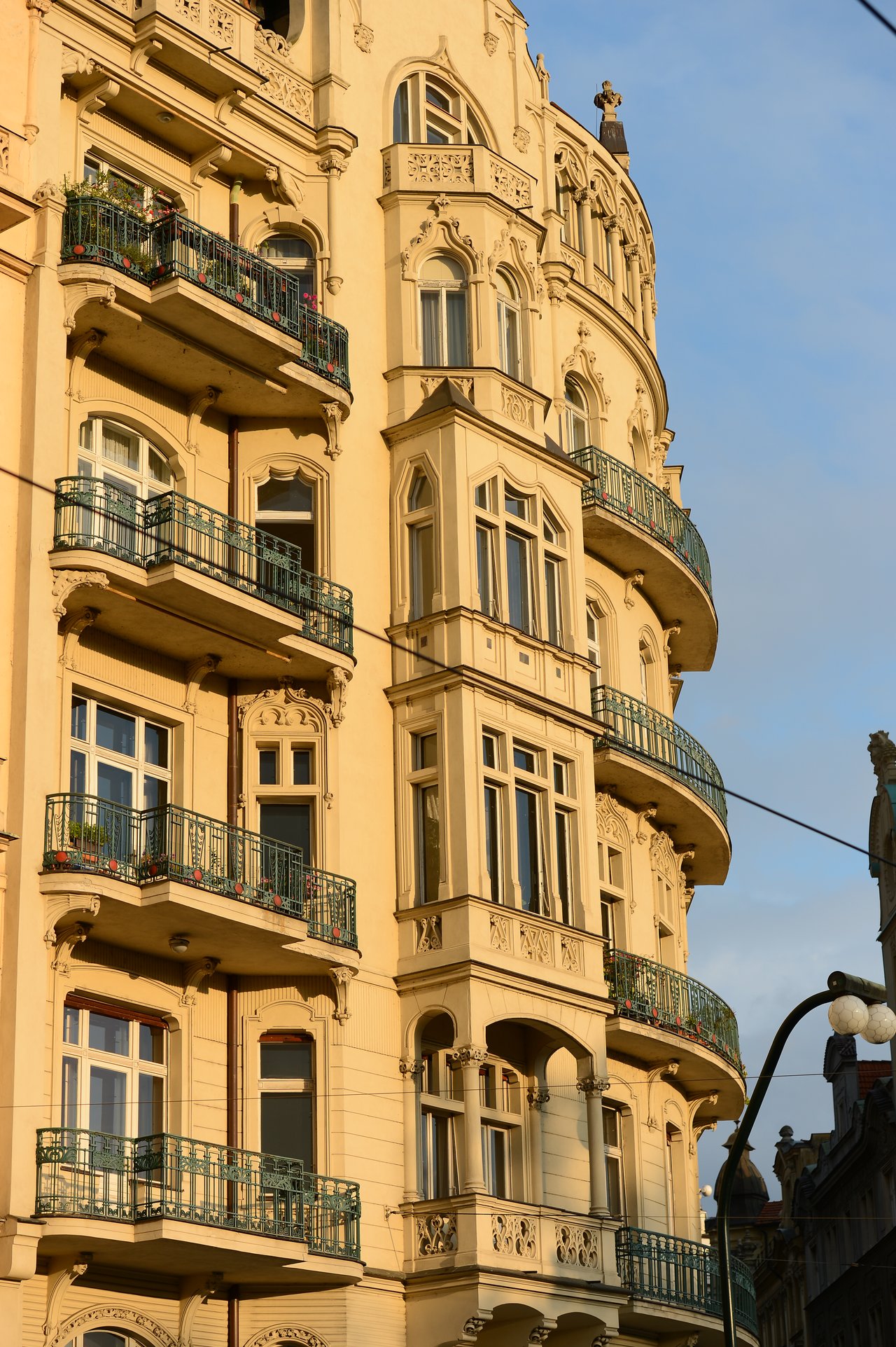 Ornate historic building in Prague with decorative balconies and large windows, illuminated by sunlight.