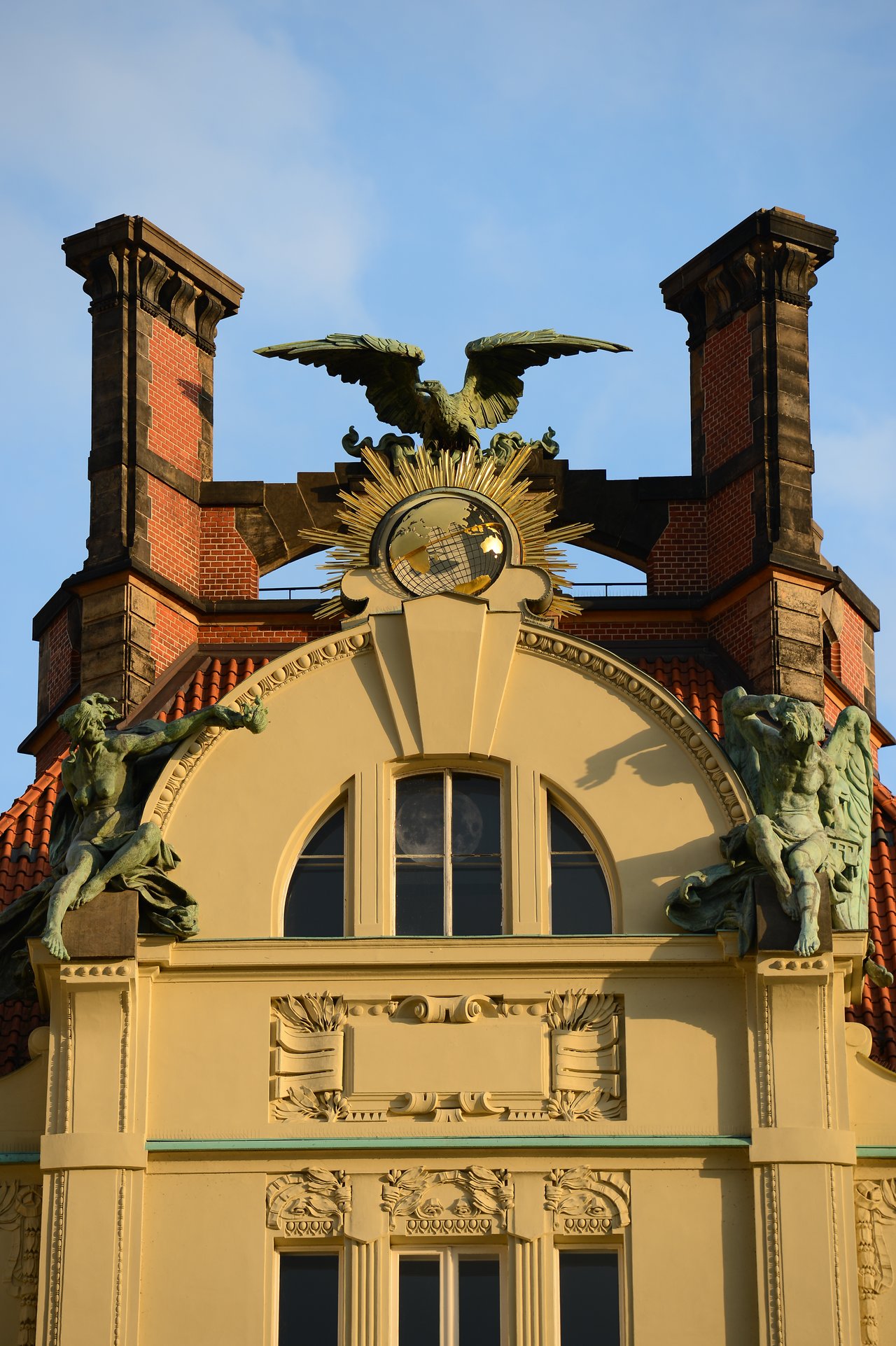 Ornate building facade in Prague with statues, a golden globe, and an eagle sculpture on the rooftop.