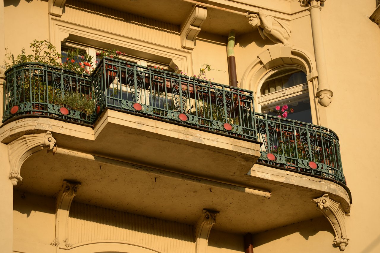 A decorative balcony with green railings and red accents, adorned with potted plants and flowers on a historic building.