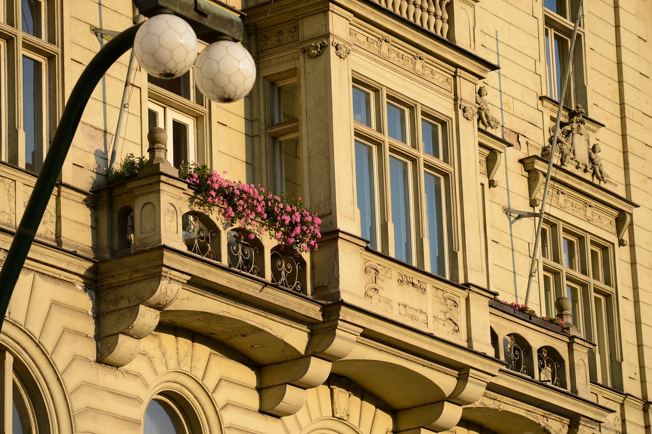 Ornate building facade with balconies, decorative railings, and pink flowers.