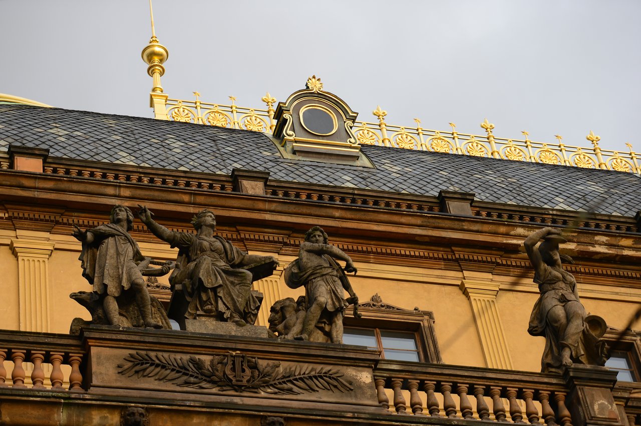 Ornate rooftop statues on a historic building in Prague, depicting figures in dynamic poses against a decorative background.