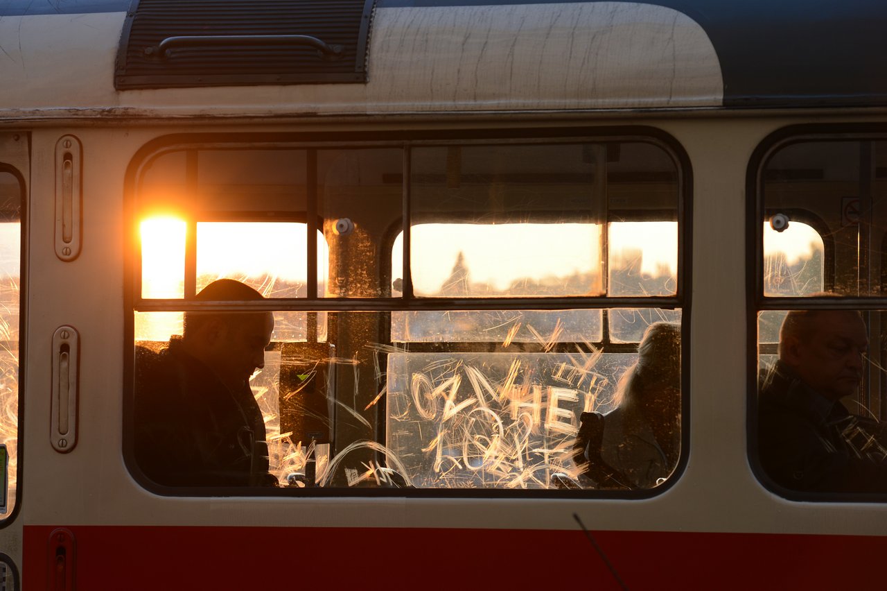 Passengers sit inside a tram with scratched windows, silhouetted against the setting sun in Prague.