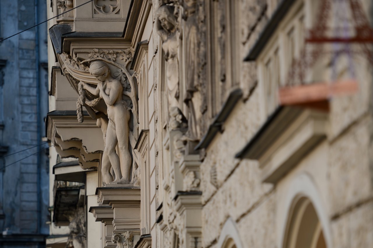 A detailed stone sculpture of a human figure holding a wreath decorates the exterior of an ornate historic building.