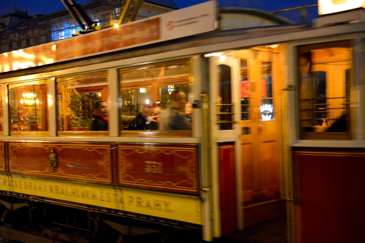 A vintage tram in Prague moves at night, with passengers visible through its warmly lit windows.