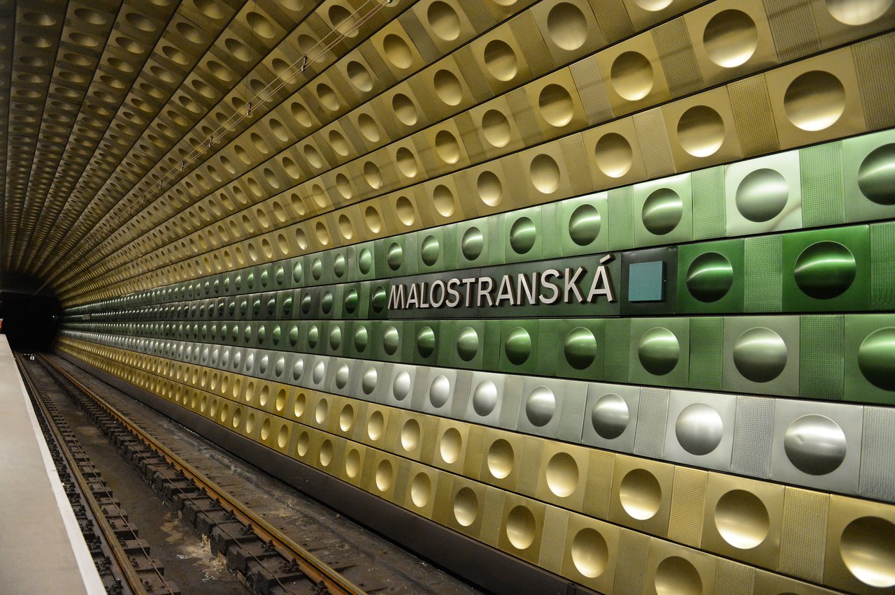 A subway platform at Malostranská station in Prague, with a patterned green and gold wall and empty tracks.