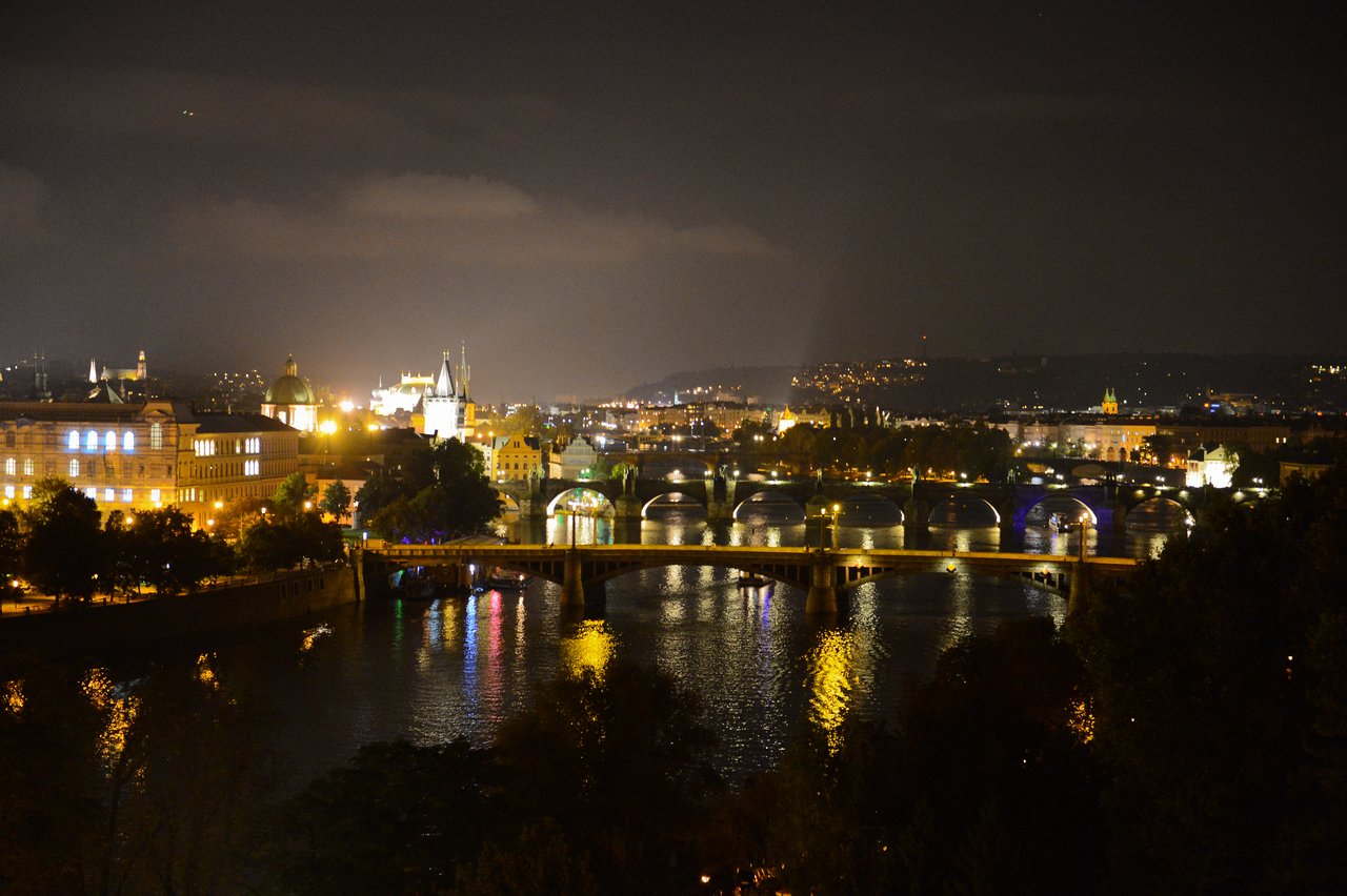 A nighttime view of Prague with illuminated bridges and buildings reflecting on the river.